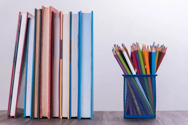 Color pencil box and stack of book on wooden table