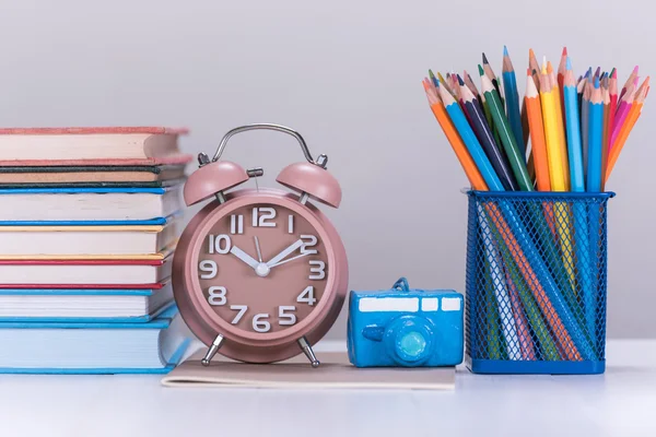 Color pencil box , alarm clock and stack of book on wooden table