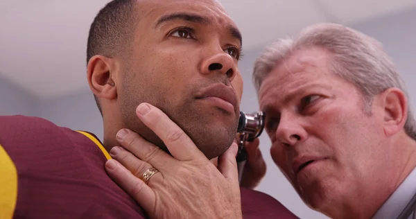 Senior doctor checking sports athlete\'s ear with an otoscope