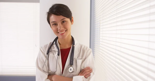 Happy Asian doctor standing by window