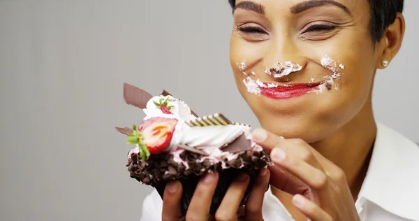 Black woman making a mess eating a huge fancy dessert