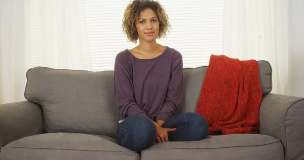 Black woman sitting on couch looking at camera
