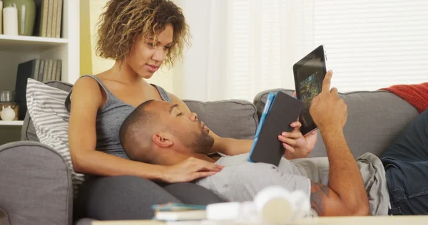 African couple using tablets on couch