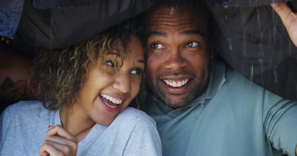 Black couple standing under coat trying not to get wet