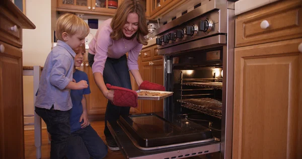 Beautiful white mother using oven mitts to remove cookie tray