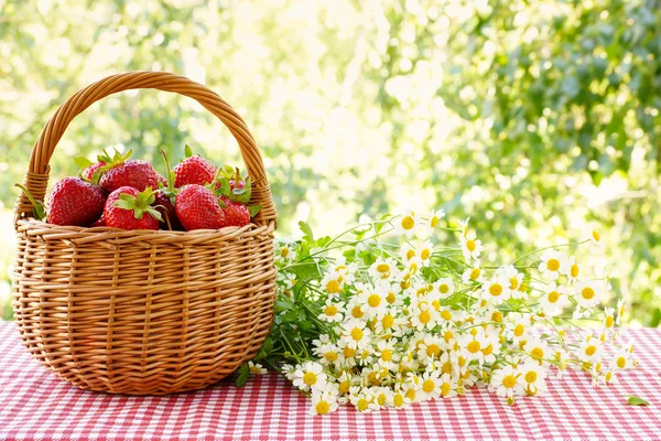 Strawberries in a basket and a bouquet of of chamomiles