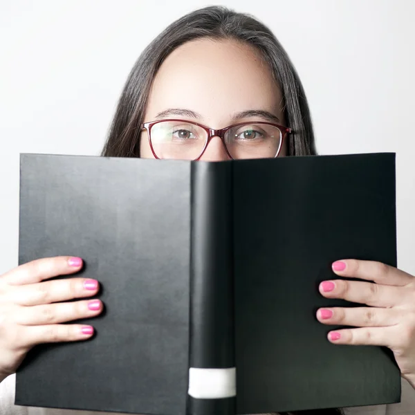 Closeup portrait of smiling young woman wearing glasses reading big black book - learning concept