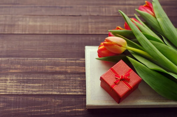 Tulips, the book and gift red box on a wooden surface.