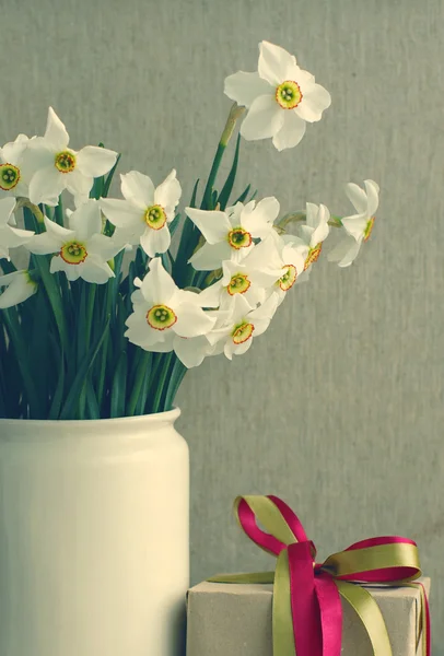 Narcissus flowers bouquet in the white vase and an gift box in vintage style.