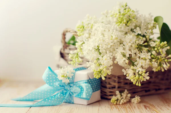 Bouquet of a white lilac in a basket and  an gift box on a wooden surface.