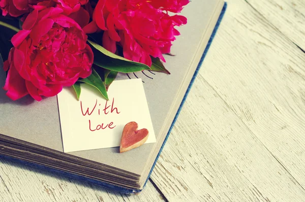 With love. Bouquet of pink peonies,one decorative heart, old photo album and the white card  with the inscription \