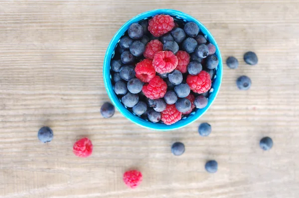 Juicy mature berries of raspberry and bilberry in a small blue bowl, top view