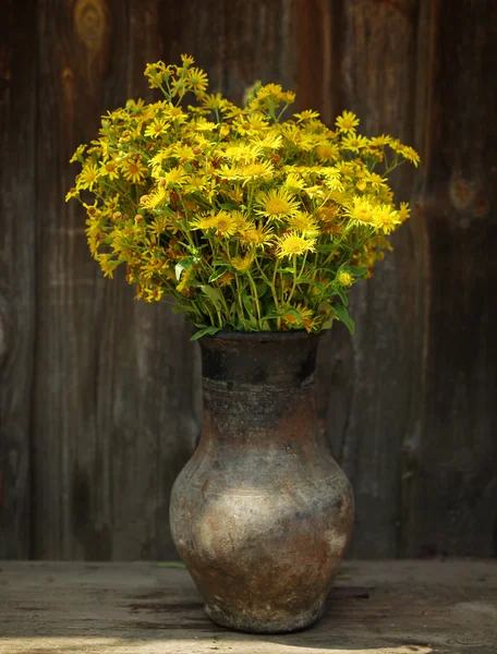 Summer field yellow flowers in an old jug on a wooden old background