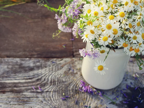 Bouquet of field camomiles in a white jug on an old wooden surface.