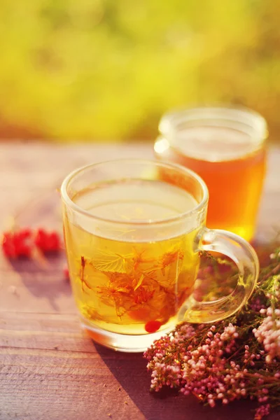 Herbal tea in a transparent glass mug and forest herbs on a wooden surface of a table.