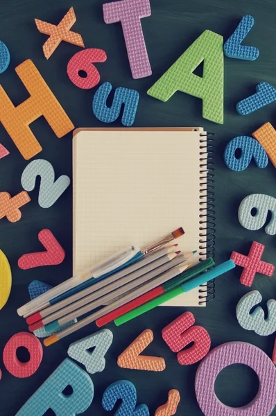 School supplies on a green table in an environment of color letters of the alphabet and numbers. Back to school background