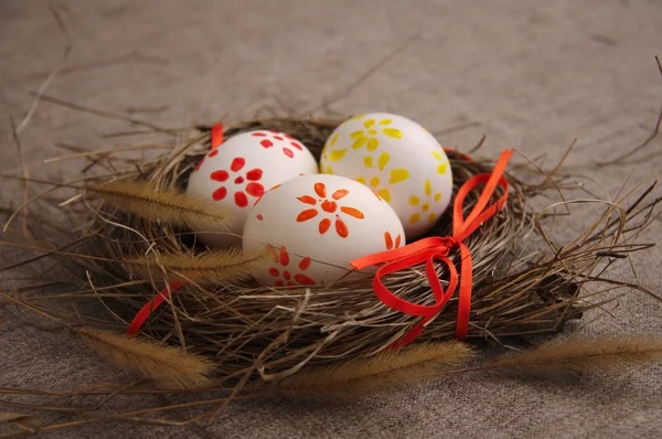 Three Easter eggs with bright drawing in a nest from a dry grass