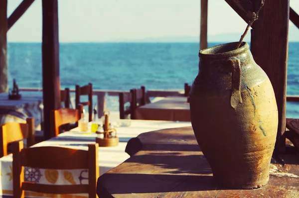 Clay Greek vase against coastal cafe and the sea. Coastal cafe.