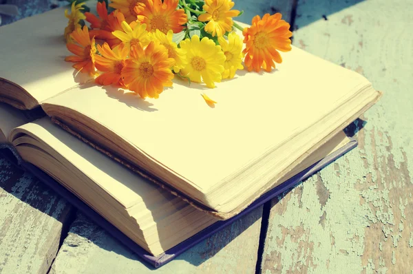 Yellow summer flowers and the old opened books on a wooden surface. Bouquet from flowers of a calendula. Medicinal herbs