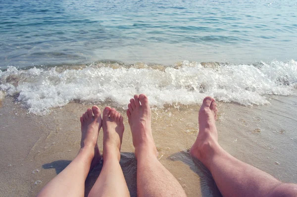 Female and male feet on a beach against the sea in a summer sunny day.