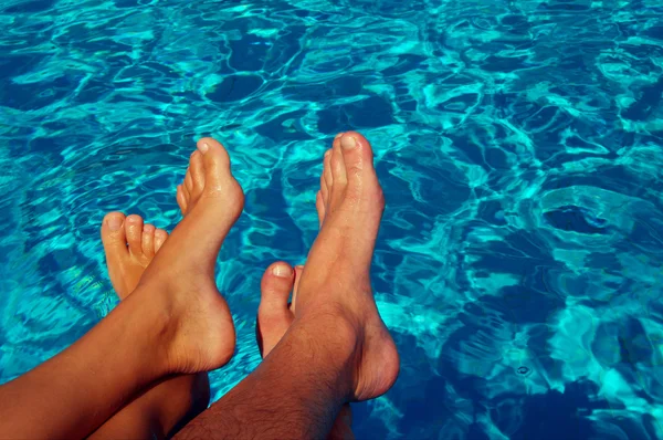 Female and male feet against blue water of the pool.