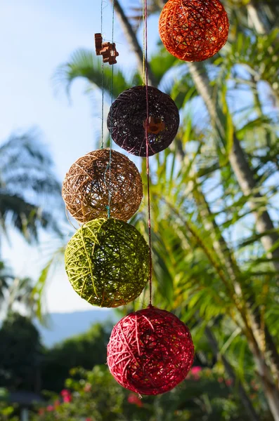 Colorful balls made of natural thread hanging in front of palm trees on a sunny day