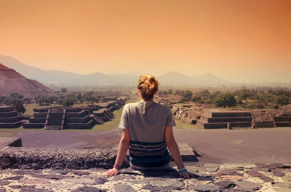 Young female sitting on top of pyramid and overlooking Teotihuacan ruins