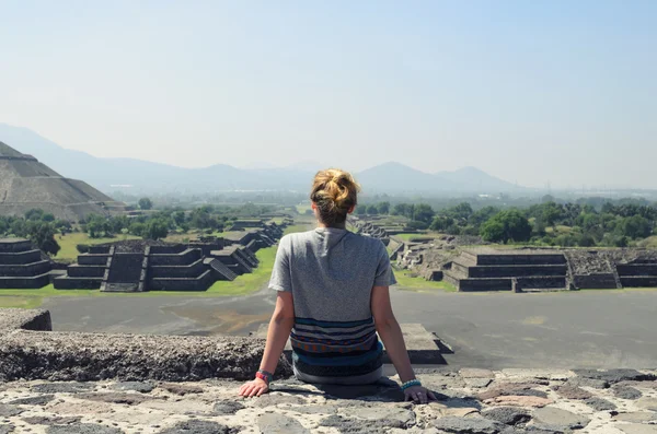 Young female sitting on top of pyramid and overlooking Teotihuacan ruins