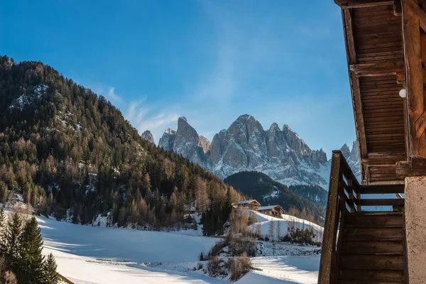 Wooden stairs of a mountain hut and the Odle mountain range with snow, blue sky with clouds, winter, Dolomites,Italy