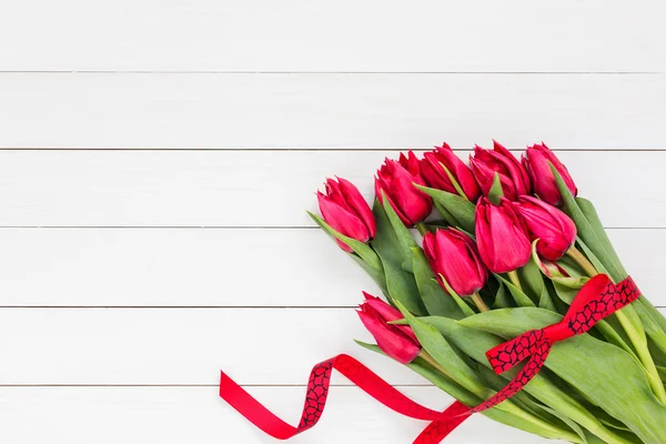 Bouquet of red tulips with red ribbon on white wooden background. Top view