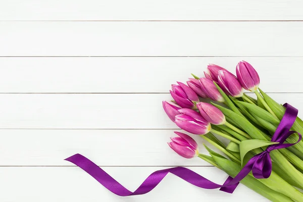 Bouquet of pink tulips decorated with purple ribbon on white wooden background. Top view, copy space