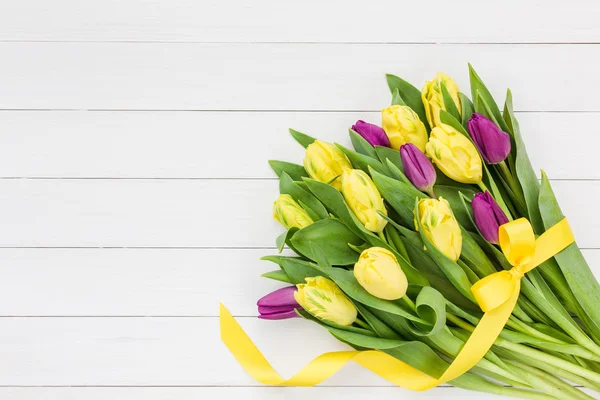 Bouquet of yellow and pink  tulips with yellow ribbon on white wooden background, copy space