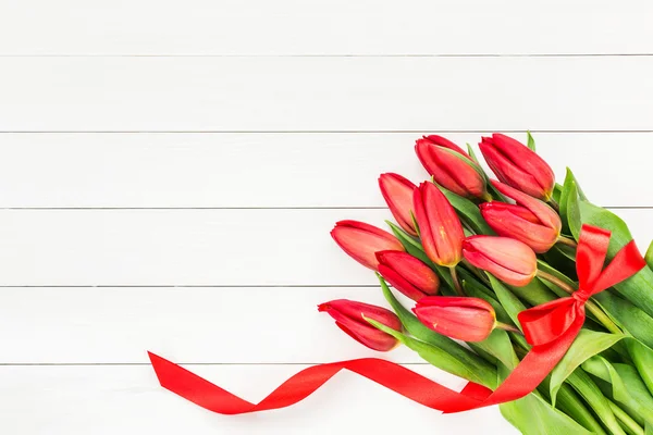 Bouquet of red tulips decorated with red ribbon on white wooden background. Top view
