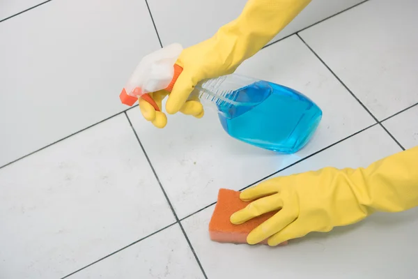 Woman in rubber gloves with detergent washes tiles.