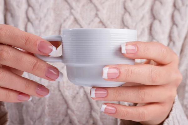 Female hands hold a coffee cup.