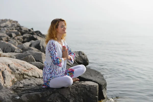 Young woman doing yoga on a rocky ocean shore