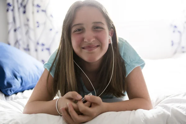 Pre teen girl is relaxing in the bed and listening to music with earphones