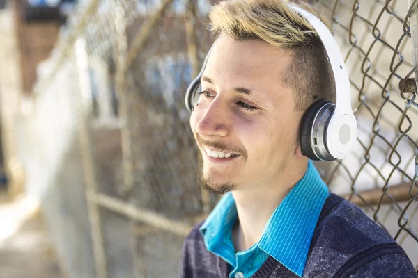 Handsome man listen to music with headphones near the fence outdoors.