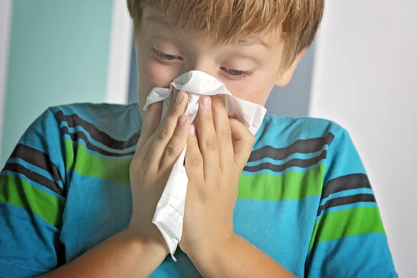 Ill boy with flu blowing nose at home