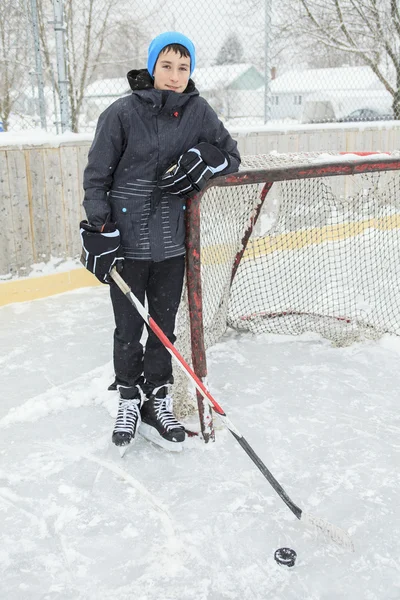 Teenager playing hockey outside on a ice rink.