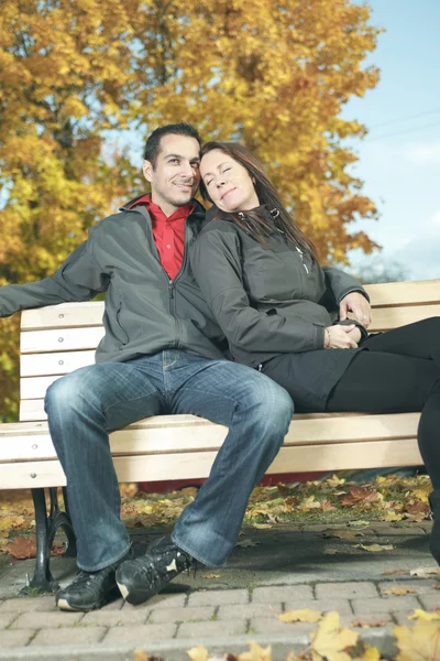 A loving couple sitting on bench in autumn background