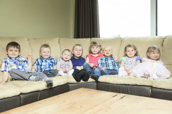 Eight little kid sit on the sofa in the living room.