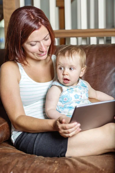 Mother and baby are looking to play and read tablet computer on the couch at home