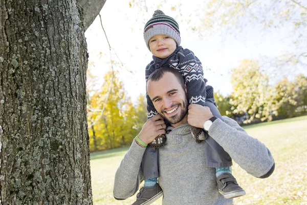 Portrait of happy father giving son piggyback ride on his shoulders in autumn park.