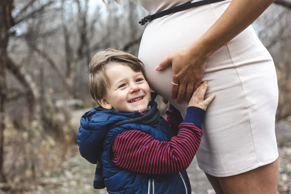 Happy child holding belly of pregnant woman in forest