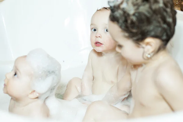 Funny little girl and her cute baby brother having fun taking bath together playing in water with foam with colorful toys after shower