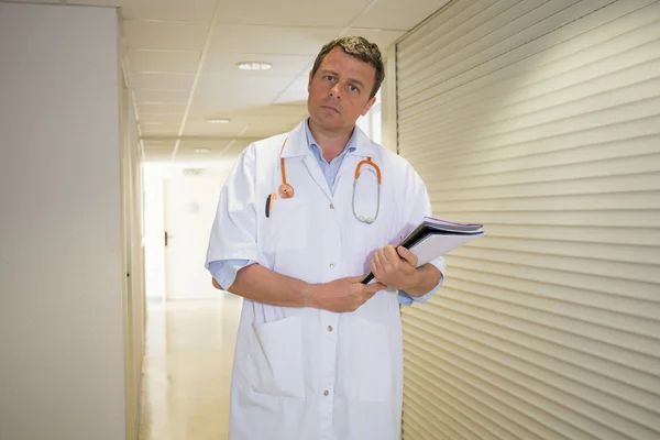 Male doctor holding reading patient`s card - next to  the wall at hospital.