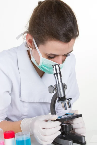 Female doctor or scientific researcher in mask using microscope in a laboratory