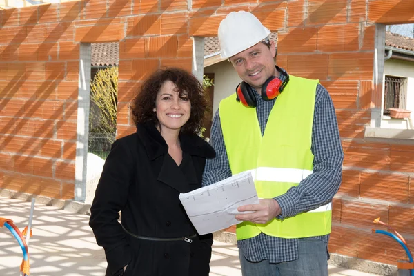 Man in hard hat, with a woman client looking plans