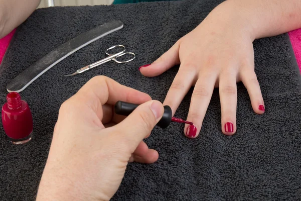 Female hands putting a varnish on nails of a girl